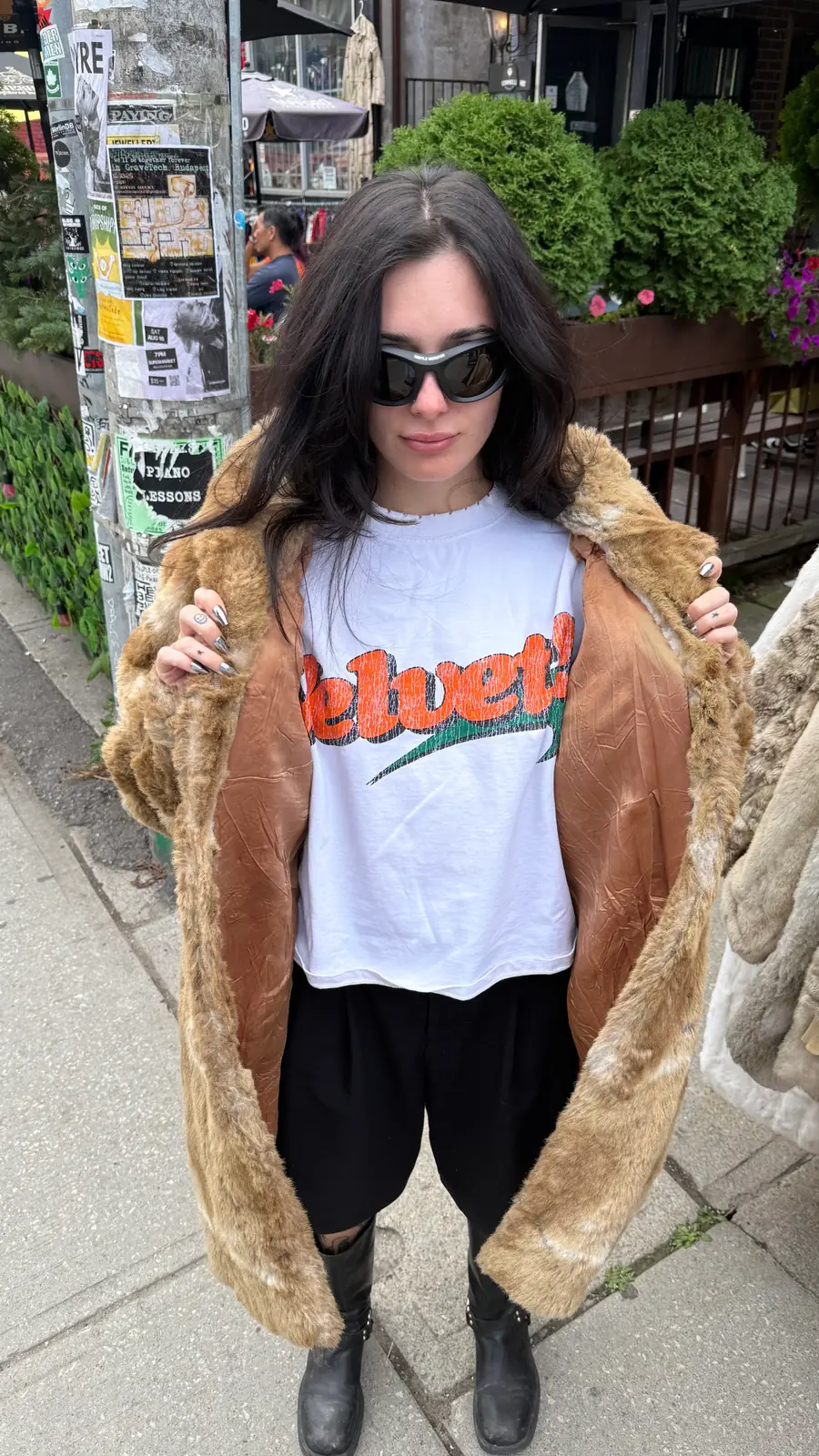 you on a sidewalk in sunglasses, fur coat open over a white velvet tee, black boots