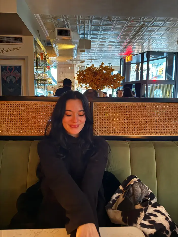 olivia sitting on a green restaurant banquette with her coat beside her