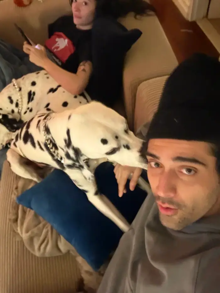 thomas in a beanie on the couch with a dalmatian sprawled across him, olivia at the far end on her phone