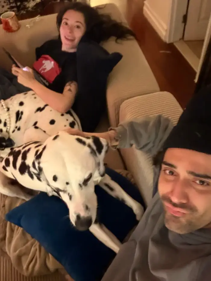 olivia laughing on the couch behind the same dalmatian, thomas at the edge of the frame