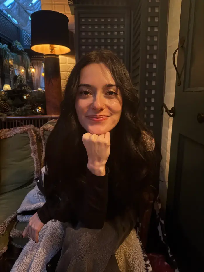 olivia in an armchair with her chin in her hand, a tall black lampshade behind her