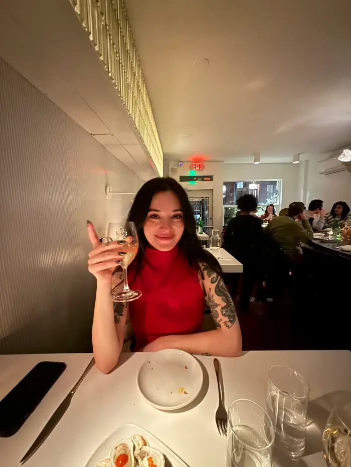 olivia in a red top at a restaurant table holding up a glass of wine